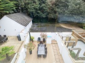 An outdoor patio with a glass table and six chairs surrounded by white walls and trees in the background at 5 Red Sails in Sandbanks