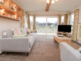 A living room with a gray sofa a coffee table and a television by large windows at Larenzo in Warton Lancashire