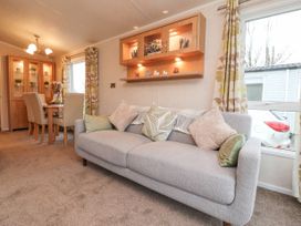 A living room with a gray sofa and multiple cushions next to a dining table with chairs and a wooden display cabinet at Larenzo in Warton Lancashire