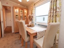 A dining area with a wooden table and four beige chairs near a window with patterned curtains at Larenzo in Warton Lancashire