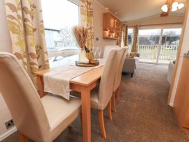 A dining area with a wooden table and four chairs next to a window and a living room with a sofa and sliding glass doors at Larenzo in Warton Lancashire