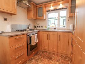 A kitchen with wooden cabinets a gas stove an oven a sink under a window and tiled floor at Larenzo in Warton Lancashire