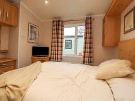 A bedroom with a bed next to a window with plaid curtains and a TV on a stand at Larenzo in Warton Lancashire