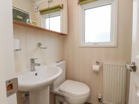 A small bathroom with a white pedestal sink, a toilet, a window, a radiator, and a mirrored cabinet above the sink at Larenzo in Warton Lancashire