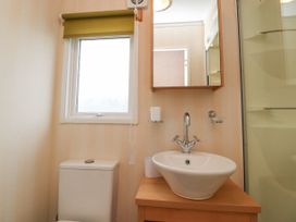 A bathroom with a toilet sink mirror small window and shower at Larenzo in Warton Lancashire