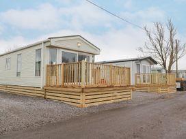 Two mobile homes with wooden decks on a gravel lot with leafless trees at Larenzo in Warton Lancashire