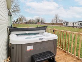 An outdoor hot tub on a wooden deck with grass field and mobile homes in the background at Larenzo in Warton Lancashire