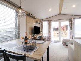 A dining table with a bottle and glasses near a TV and a seating area with windows and curtains at Giorgio in Warton Bank near Warton Lancashire
