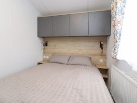 A bedroom with a double bed gray bedding overhead cabinets wall lamps and a window with patterned curtains at Giorgio Warton Bank near Warton Lancashire