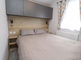 A bedroom with a double bed two bedside tables wall cabinets and a window with patterned curtains at Giorgio Warton Bank near Warton Lancashire