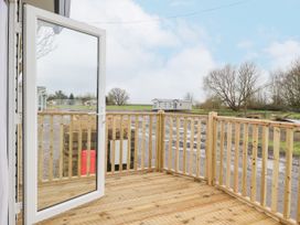 A wooden deck with railing and an open glass door overlooking a field with a mobile home and trees at Giorgio in Warton Bank near Warton Lancashire