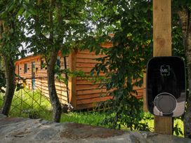 An electric vehicle charger with a wooden building behind at Owl Lodge in Menheniot