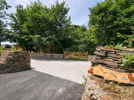 An outdoor area with a stone wall and wooden sign at Owl Lodge in Menheniot