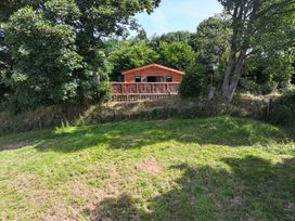 A log cabin with decking surrounded by trees at Owl Lodge in Menheniot
