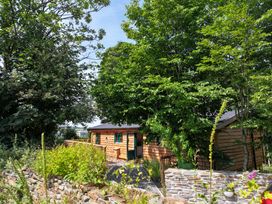 A wooden cabin surrounded by trees and plants at Owl Lodge in Menheniot