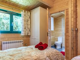 A bedroom with a window and a bathroom door at Owl Lodge in Menheniot