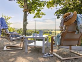 A deck with two chairs and a table overlooking a scenic view at Owl Lodge Menheniot