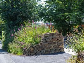 A stone wall with flowers and trees at Owl Lodge Menheniot