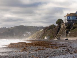 A beach with a house on a cliff and ocean waves at Owl Lodge in Menheniot