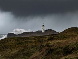 A lighthouse on a rocky shore with waves at Owl Lodge in Menheniot