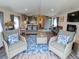 A living room with two armchairs and a sofa with patterned cushions a coffee table and a kitchen in the background at The Hoot in Great Finborough near Stowmarket
