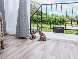 Two rabbit sculptures on a wooden floor next to a glass door with gray patterned curtains and an outdoor patio with a table and chairs at The Hoot in Great Finborough near Stowmarket