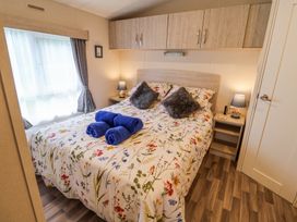 A bedroom with a bed with floral bedding blue towels on the bed two bedside tables with lamps and overhead cabinets at The Hoot in Great Finborough near Stowmarket