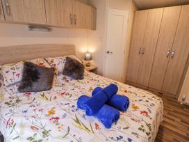 A bedroom with a floral bedspread blue towels on a bed fur pillows wooden cabinets and a bedside table lamp at The Hoot in Great Finborough near Stowmarket