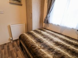 A bedroom with a bed covered with a brown furry blanket a wooden wardrobe a window with curtains and a radiator on the wall at The Hoot in Great Finborough near Stowmarket