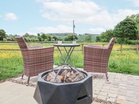 An outdoor patio with two wicker chairs a small round table with mugs and a fire pit with wood at The Hoot in Great Finborough near Stowmarket