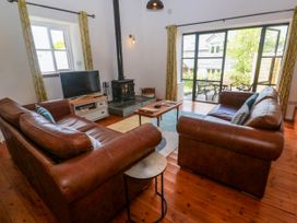 A living room with two brown leather sofas a wood stove a television and sliding glass doors leading to a garden at Joe's Barn in Mullion