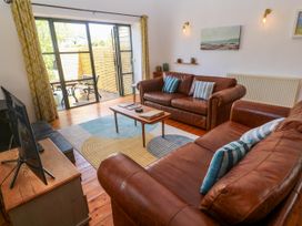 A living room with brown leather sofas a wooden coffee table a television and glass doors opening to a patio at Joe's Barn in Mullion