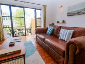 A living room with a brown leather sofa, blue striped cushions, a wooden coffee table, and glass doors leading to an outdoor area with a table and two chairs at Joe's Barn in Mullion