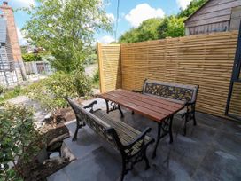 An outdoor patio area with a wooden table and two benches with metal frames and a wooden privacy fence at Joes Barn in Mullion
