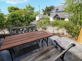 An outdoor seating area with a wooden table and two benches on a tiled patio near a road and houses at Joes Barn in Mullion