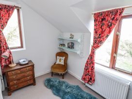A bedroom corner with a chair, bookshelf, and window at Pencestyll in Cardigan