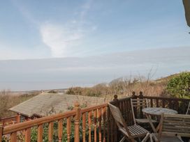 A wooden balcony with chairs and a table overlooking trees and rooftops at Bayview 23 in West Quantoxhead