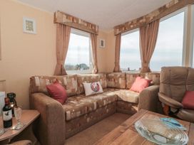 A living room with a patterned brown sofa red cushions a leather chair and a wooden table with a glass bowl at Bayview 23 in West Quantoxhead