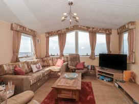 A lounge with a corner sofa armchair coffee table television and books at Bayview 23 in West Quantoxhead