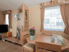 A dining area with wooden table and chairs next to a window with curtains and a small shelf with decorative items and a television in a living room at Bayview 23 West Quantoxhead