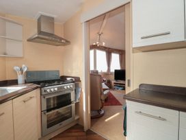 A kitchen with a stove and utensils and a view into a living room with a TV and armchair at Bayview 23 in West Quantoxhead