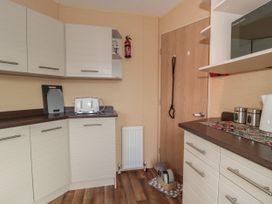A kitchen with white cabinets brown countertops a white toaster a cutting board a microwave a white kettle and a dog feeding area at Bayview 23 in West Quantoxhead