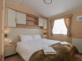 A bedroom with a double bed, bedside tables, wall cabinets, and a window with curtains at Bayview 23 in West Quantoxhead
