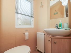 A small bathroom with a toilet paper holder under a window a radiator a sink with a mirror above and soap at Bayview 23 in West Quantoxhead