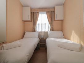 A bedroom with two single beds separated by a small wooden nightstand with a lamp under a window with curtains at Bayview 23 in West Quantoxhead
