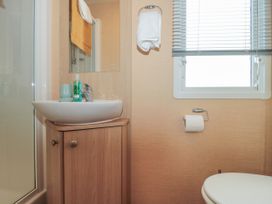 A bathroom with a sink on a wooden cabinet a mirror a towel hanging a window with blinds and a toilet at Bayview 23 West Quantoxhead