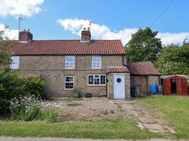 A stone house with red tiled roof a white door and garden area at 2 Beck Houses in Menethorpe near Malton