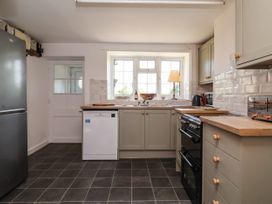 A kitchen with grey cabinets, wood countertops, a black stove, fridge, dishwasher, tiled floor, and a window with a lamp at 2 Beck Houses in Menethorpe near Malton