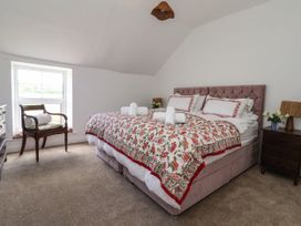 A bedroom with a double bed covered with a floral quilt towels on the bed a wooden chair near a window and a bedside table with a lamp and flowers at 2 Beck Houses in Menethorpe near Malton