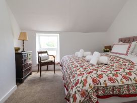 A bedroom with a bed covered by a floral quilt and folded towels on it a wooden chair by the window and a chest of drawers with a lamp at 2 Beck Houses in Menethorpe near Malton